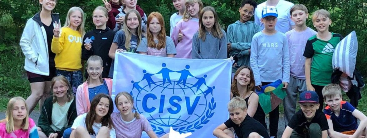 Group of people smiling and holding a CISV-flag